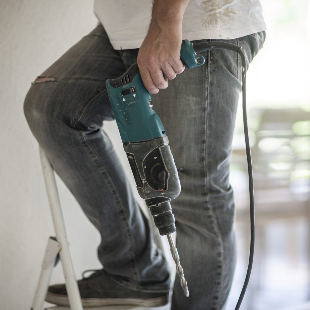Builder holding drill on ladder