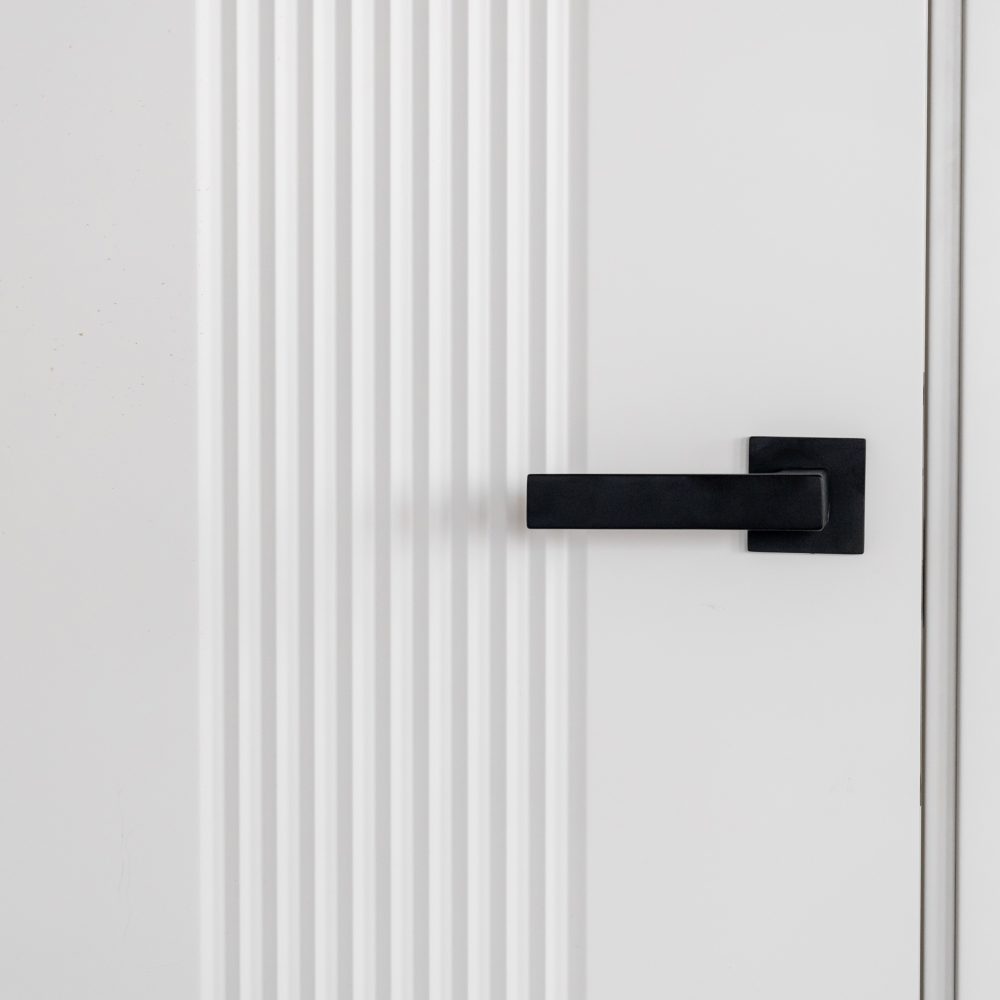 Modern black door handle on white wooden door in interior. Knob close-up elements. Door handle, fittings for interior design. Element of interior design