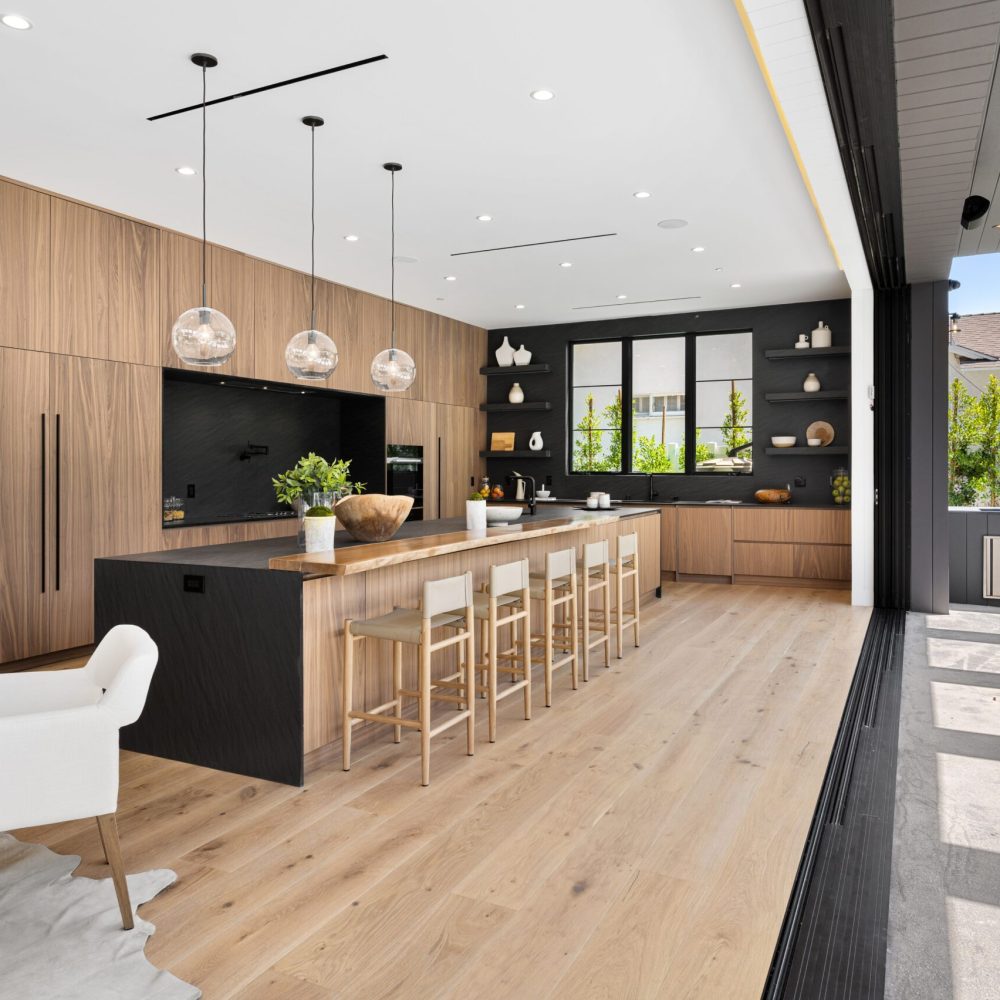 Modern open-concept kitchen with wooden cabinets, large island, and floor-to-ceiling windows leading to an outdoor patio.